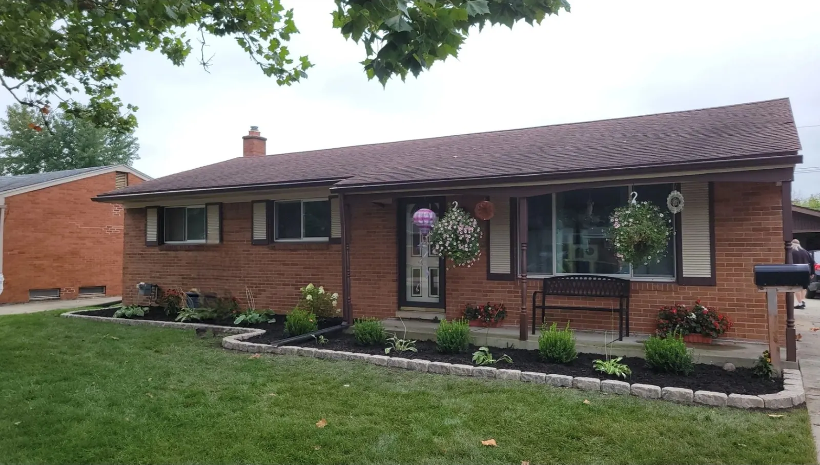 A brick ranch home with a mown lawn and a mulch bed edged with stone blocks and planted with flowers