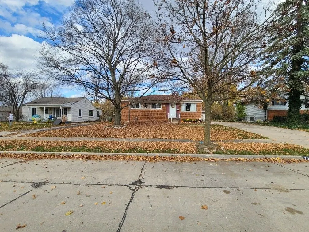 A street of homes and bare autumn trees with fallen leaves scattered across the lawn