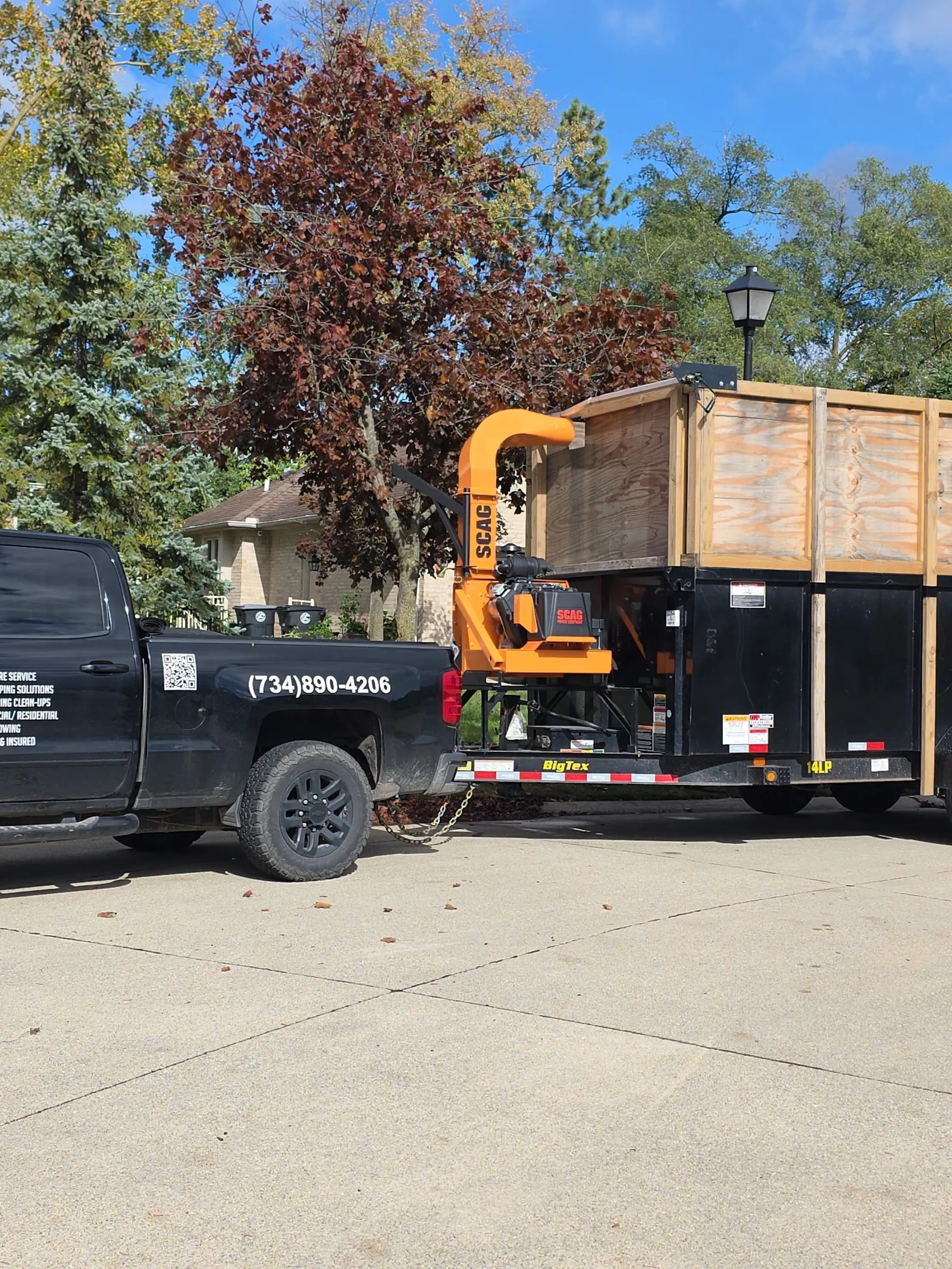 Black pickup truck hitched to a trailer carrying an orange wood chipper and a wooden-sided dump box