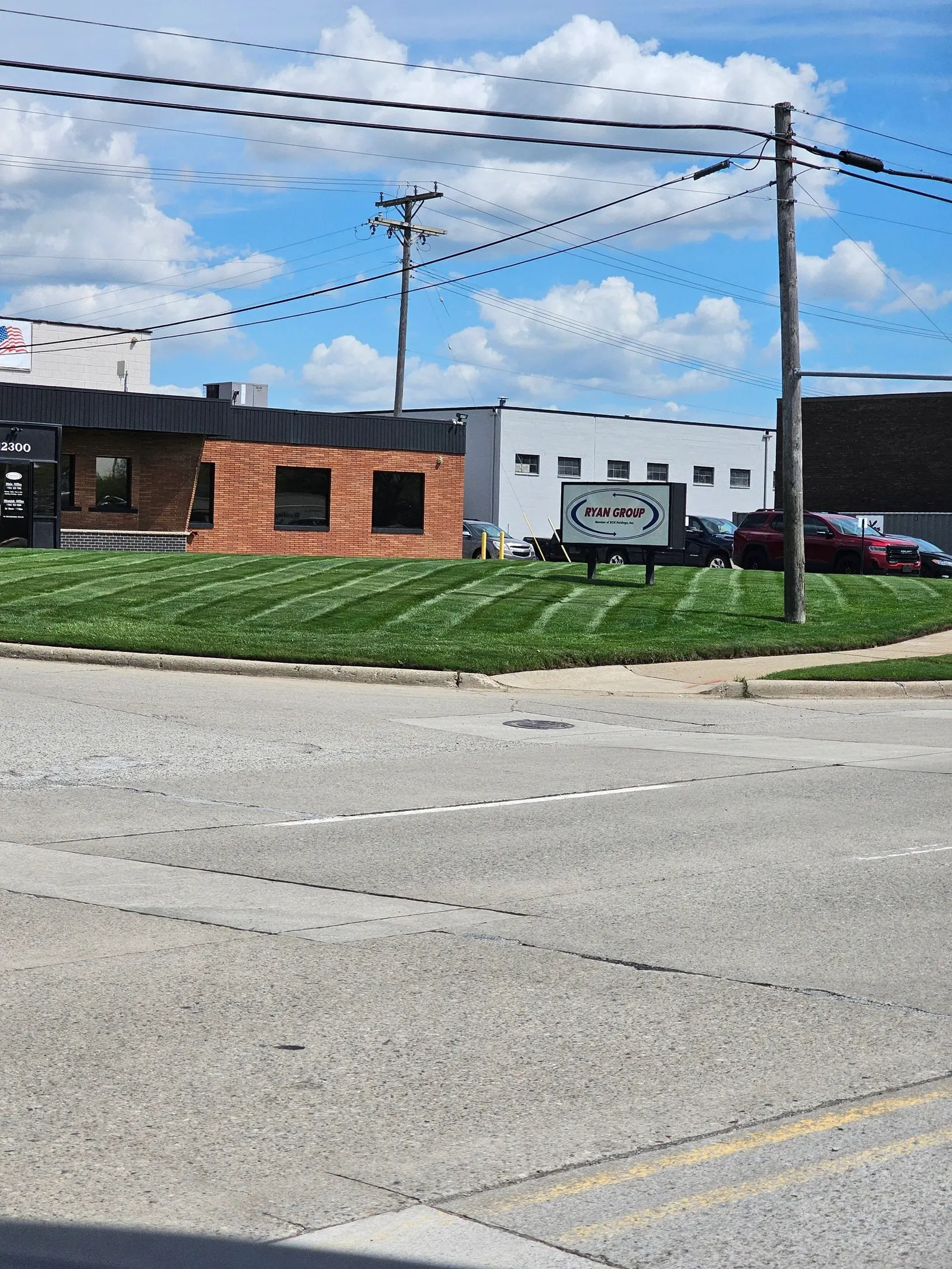 A freshly mown lawn along the street in front of a commercial building with a sign and a parking lot
